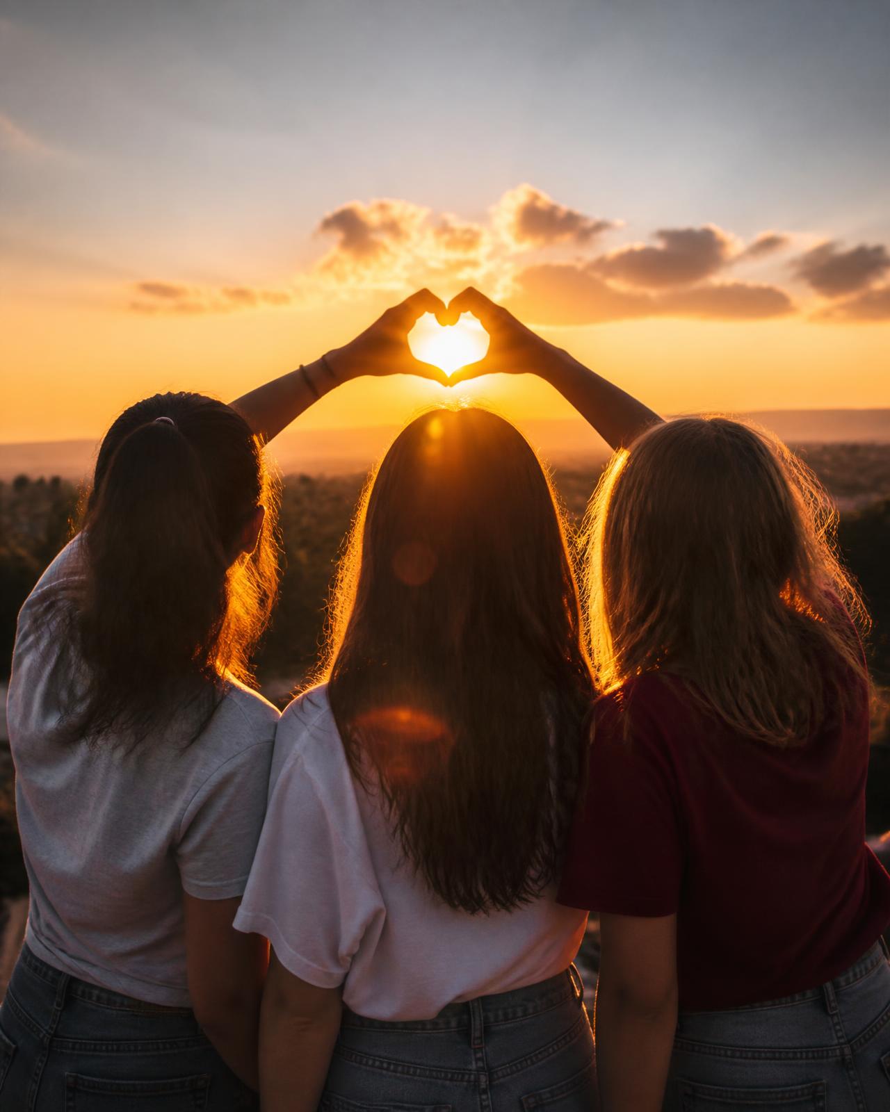 A group of friends at sunset, seen from behind, with arms raised together